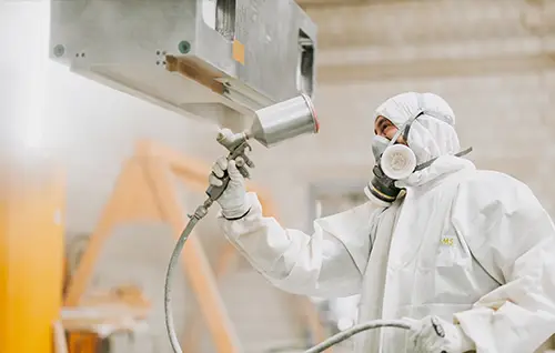 Mitarbeiter in Schutzanzug beim Lackieren eines Maschinenbauteils