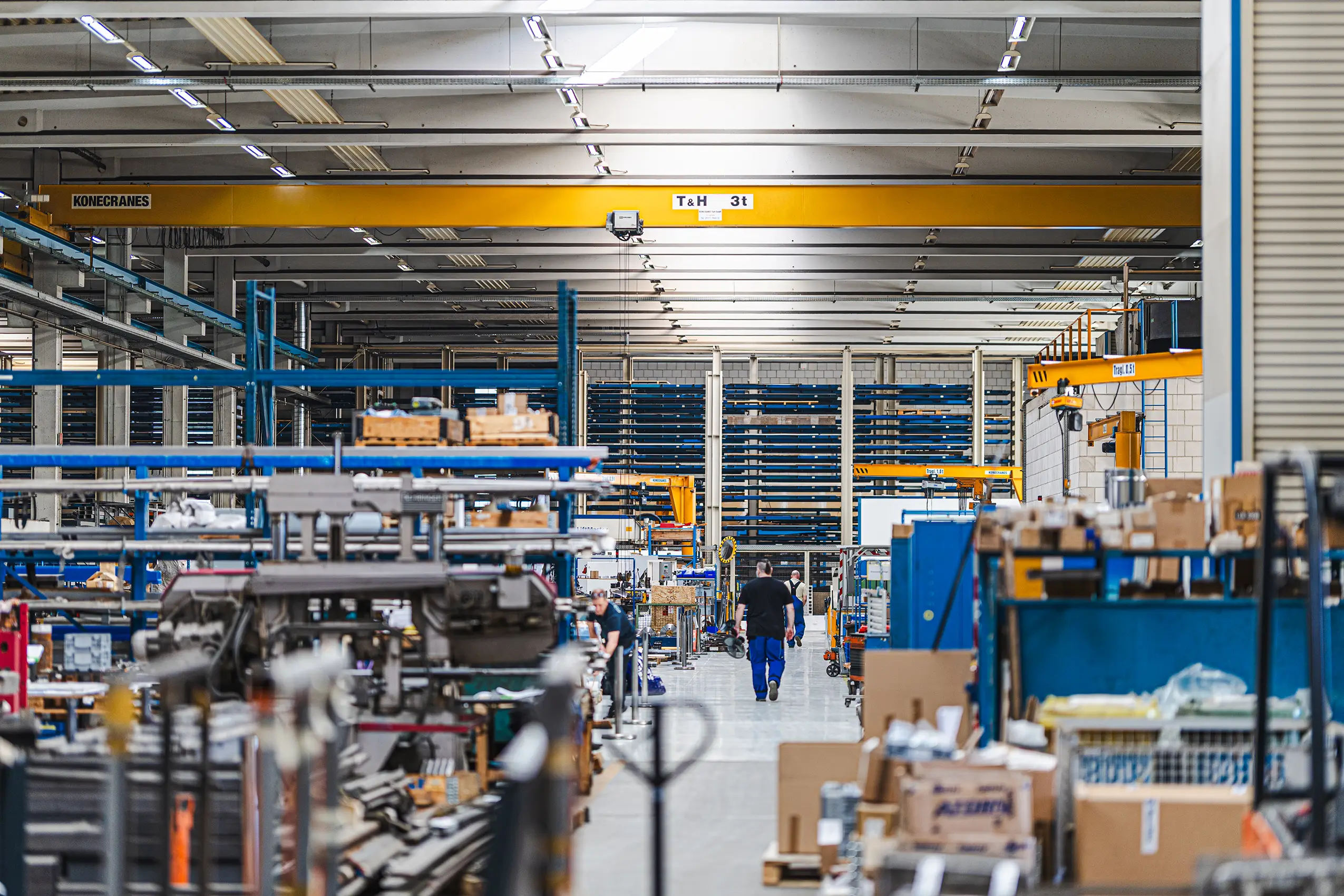 Blick in die Produktionshalle mit Lagerregalen, Kran und Mitarbeitern