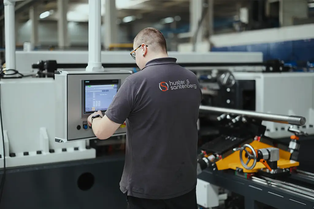 Mitarbeiter von Huster & Santenberg steuert eine moderne Produktionsanlage über ein digitales Bedienpanel in der Fertigungshalle.