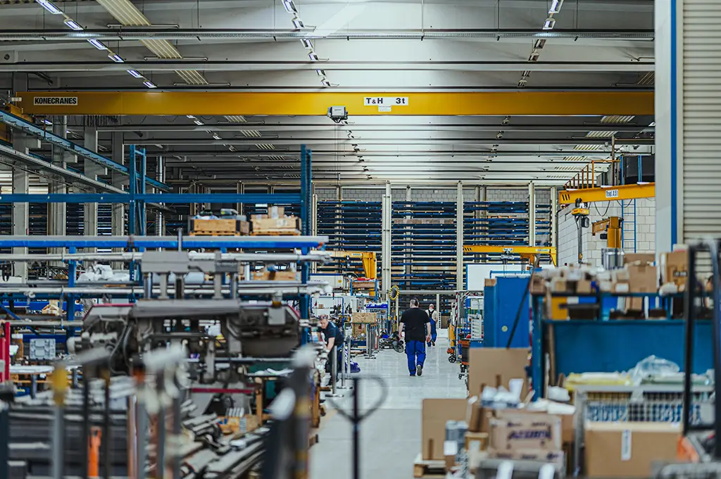 Blick in die Produktionshalle mit Lagerregalen, Kran und Mitarbeitern